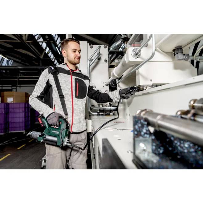 Eine Person, die einen Elektroschrauber an Industriemaschinen in einer Fabrikumgebung verwendet, umgeben von Ausrüstung und Lagerbehältern.