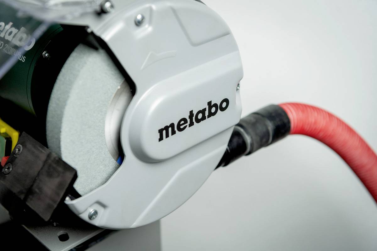Ein professioneller Schleifstein mit der Aufschrift 'metabo', verbunden mit einem roten Schlauch, verwendet zum Schärfen von Werkzeugen.