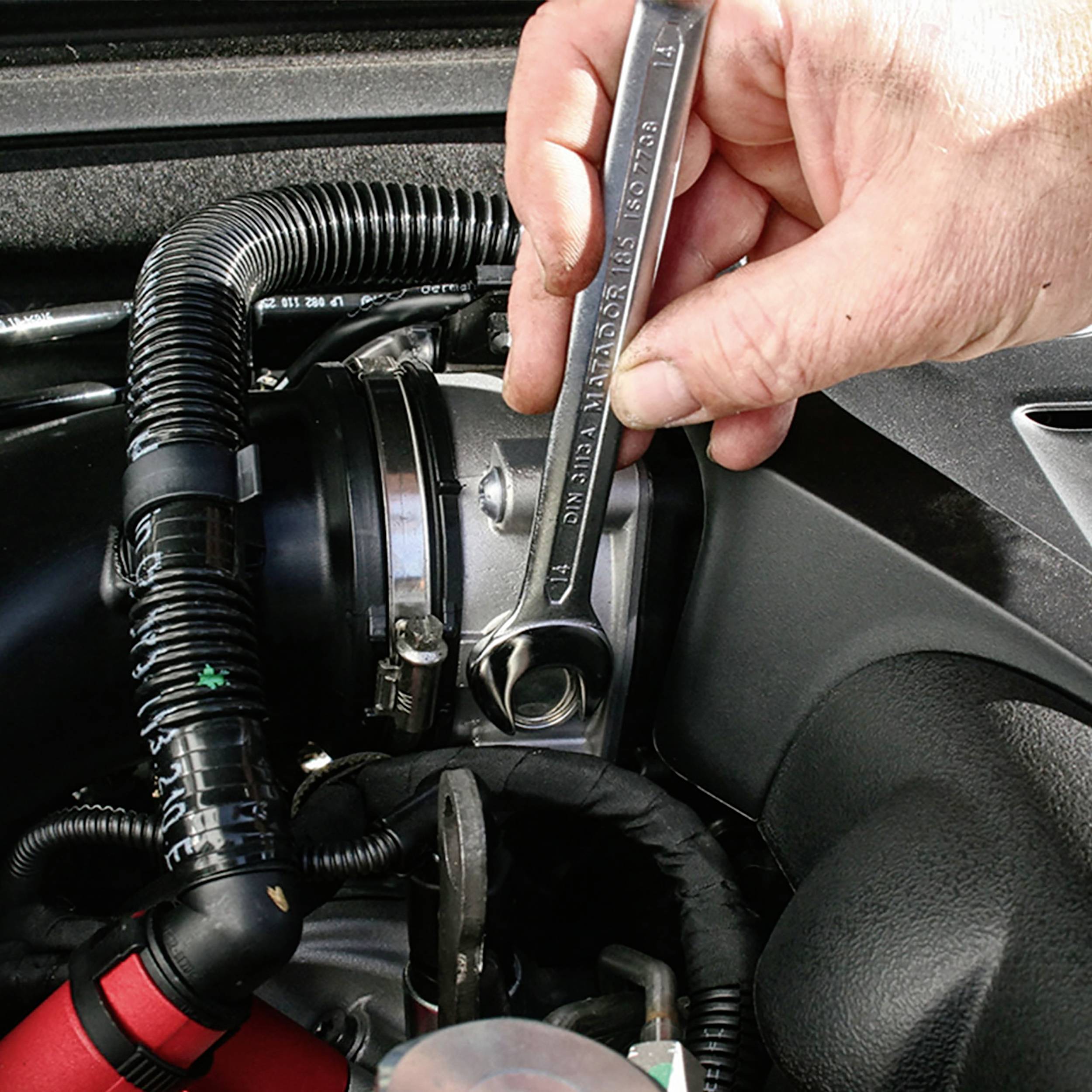 Ein Mechaniker zieht eine Schraube im Motorraum eines Autos mit einem Schraubenschlüssel an, um Wartungsarbeiten durchzuführen.