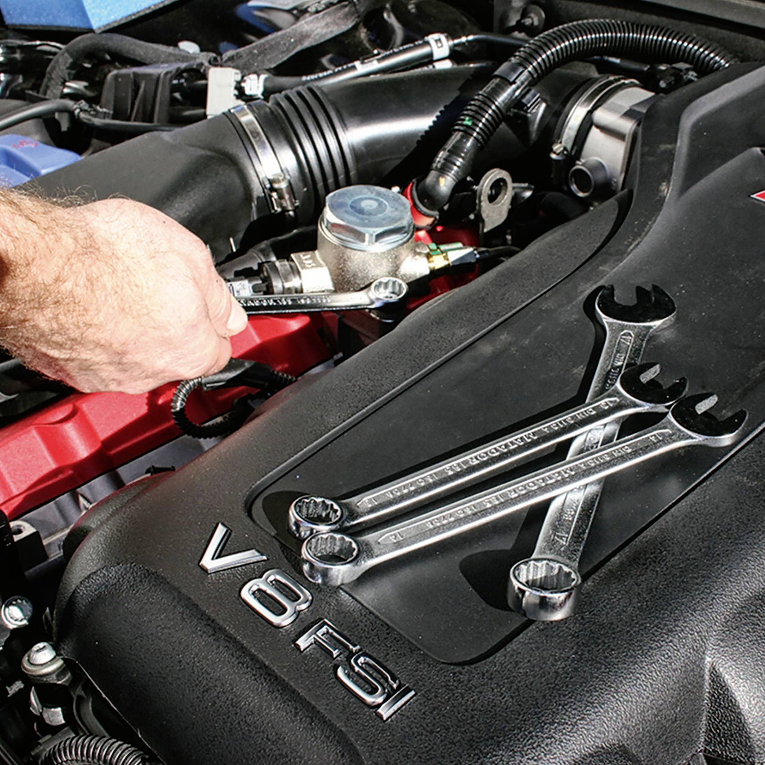 Eine Person führt Wartungsarbeiten an einem V8-Motor durch, indem sie einen Schraubenschlüssel verwendet. Mehrere Werkzeuge liegen bereit.