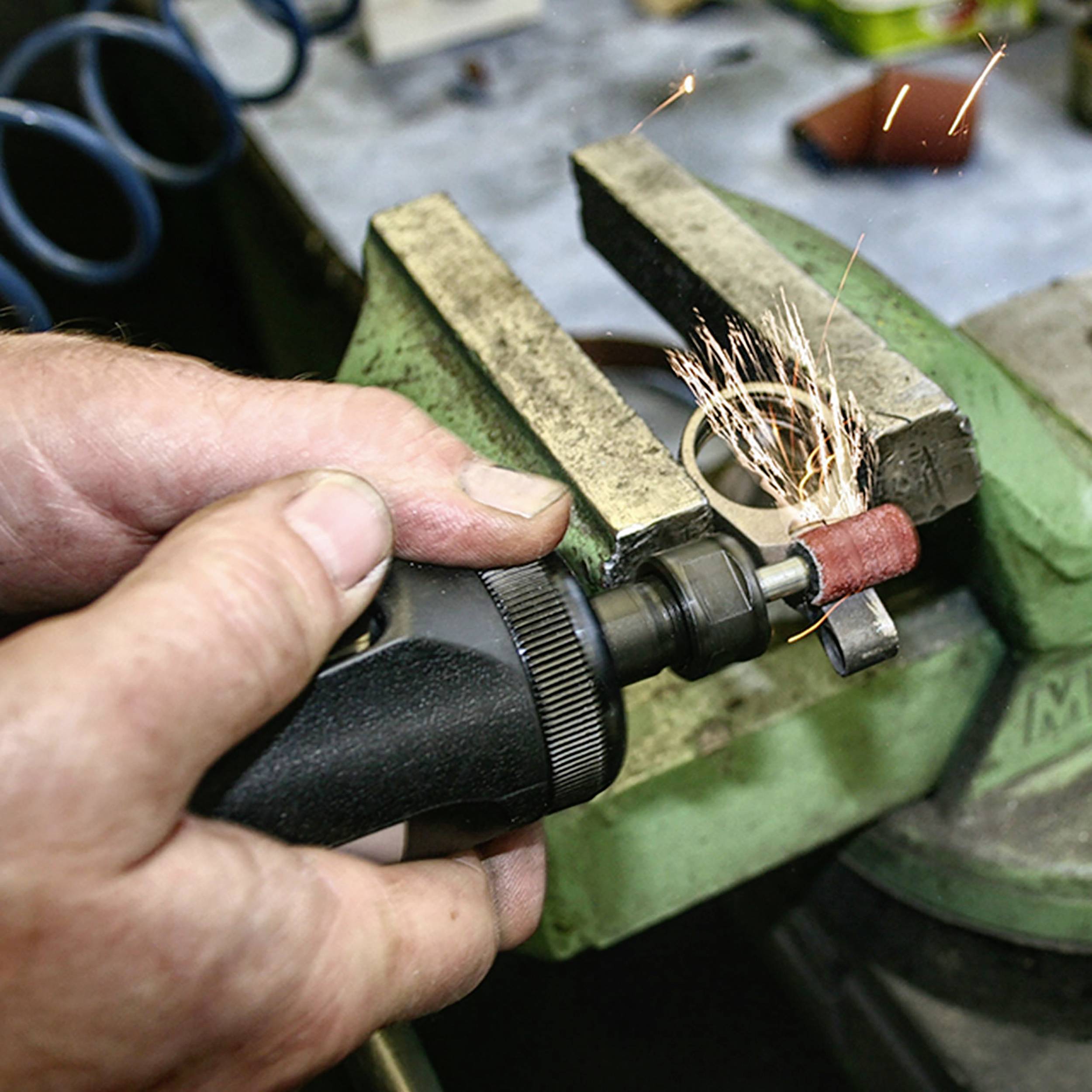 Eine Person verwendet einen elektrischen Schleifer, um einen kleinen Metallgegenstand in einer Werkstatt zu bearbeiten, Funken fliegen.