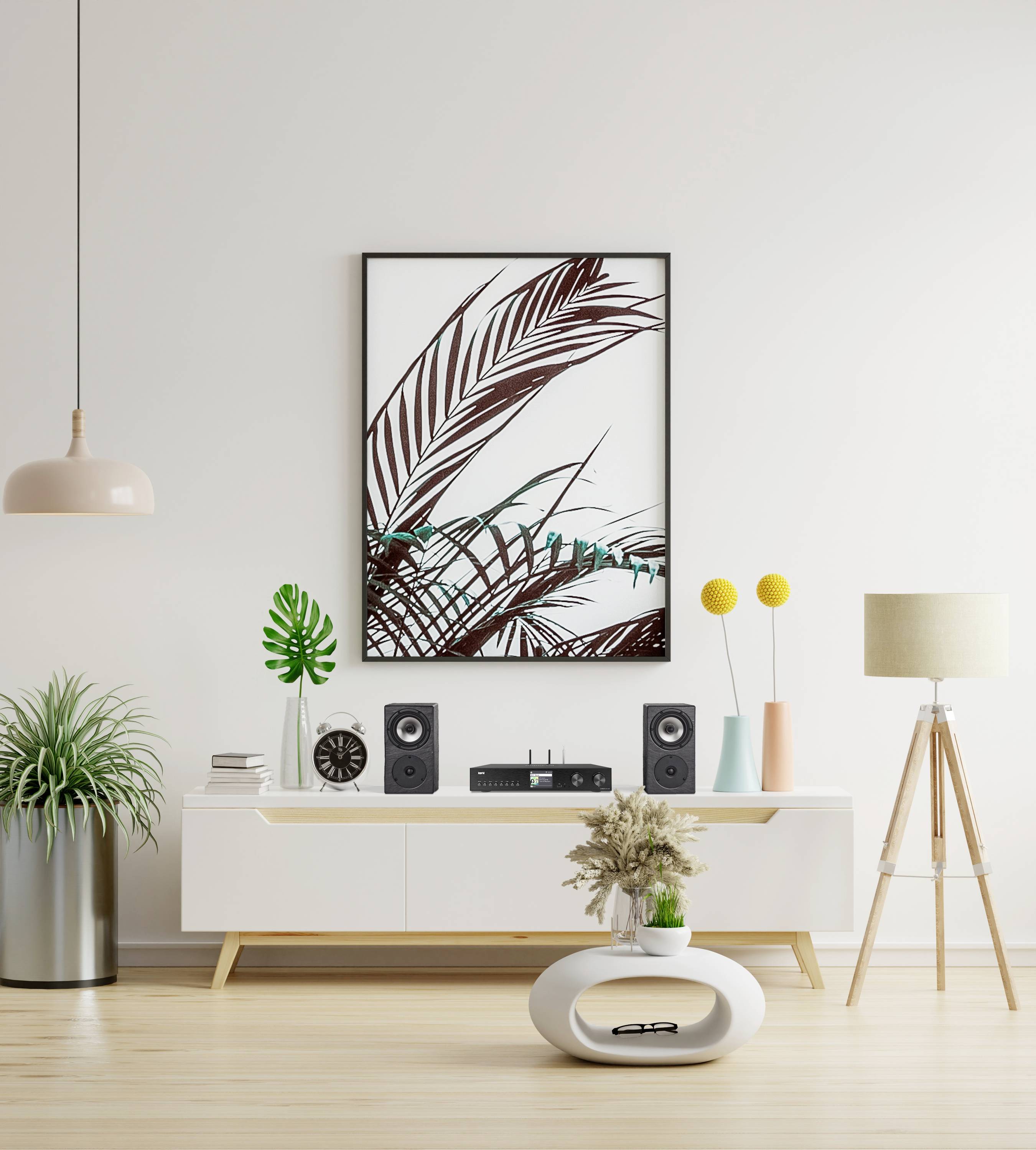 Modernes Wohnzimmer mit minimalistischer Dekoration: Weiße Kommode, Pflanzen, Lautsprecher und ein Bild mit Palmenmotiv an der Wand.