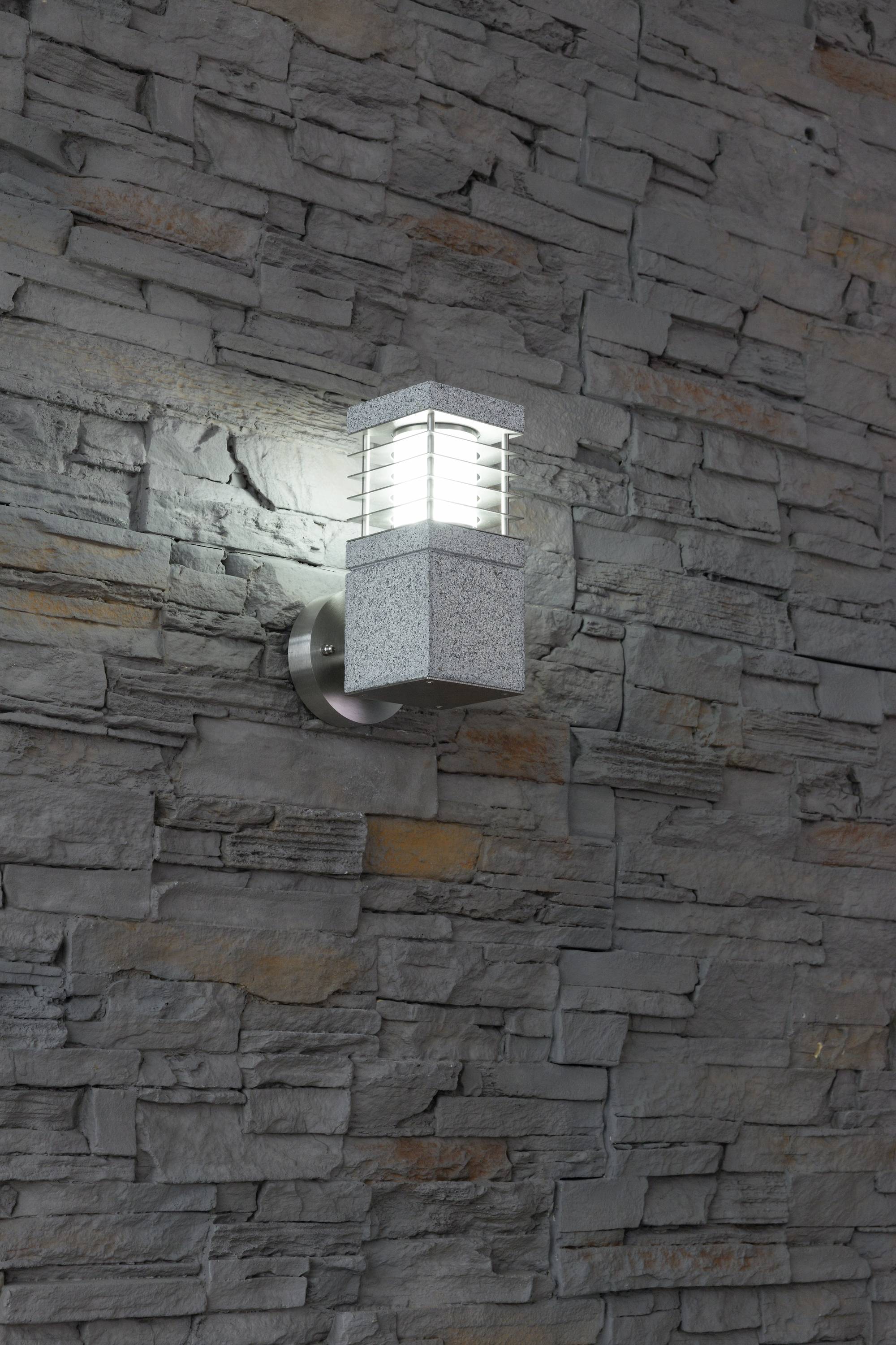 Wandleuchte in modernem Design an einer grauen Ziegelwand, eingeschaltet und Licht abstrahlend.