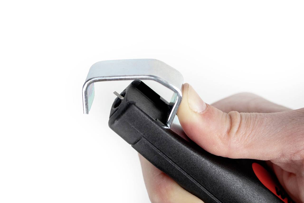 Hand hält einen Hefterentferner. Metallkrallen sind über die Spitze gebogen, um eine Heftklammer zu entfernen.