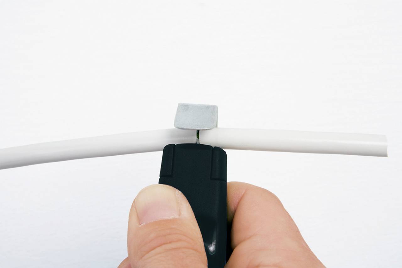 Eine Nahaufnahme einer Hand, die ein Werkzeug verwendet, um ein Kabel zu schneiden. Das Werkzeug ist schwarz, und das Kabel ist weiß.