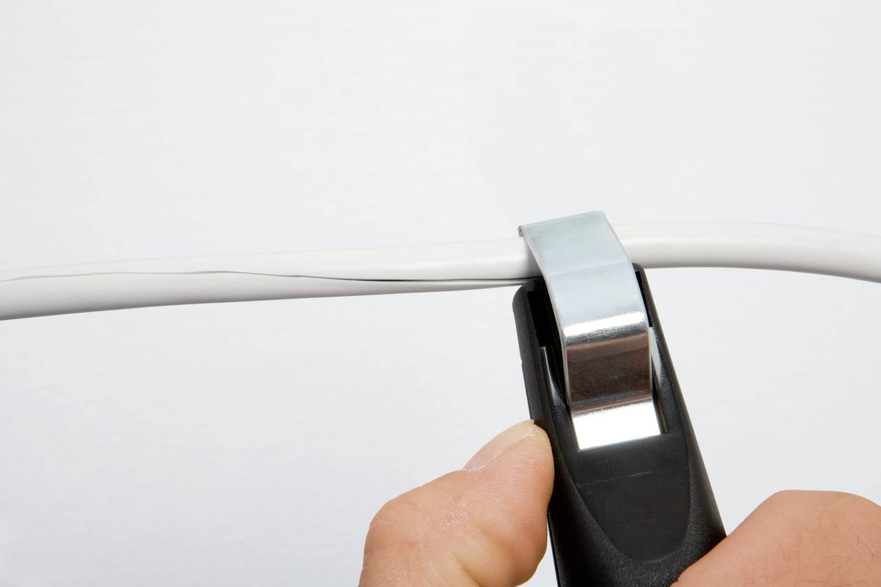 Eine Hand benutzt einen Entisolierer, um die Isolierung von einem elektrischen Kabel zu entfernen.