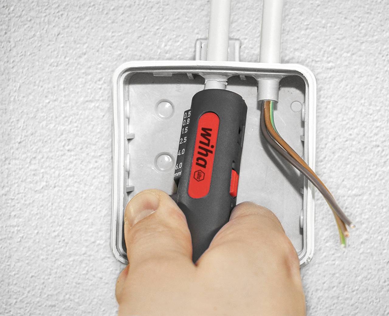 Eine Hand hält einen Spannungsprüfer an einem offenen elektrischen Anschlusskasten mit sichtbaren Kabeln.