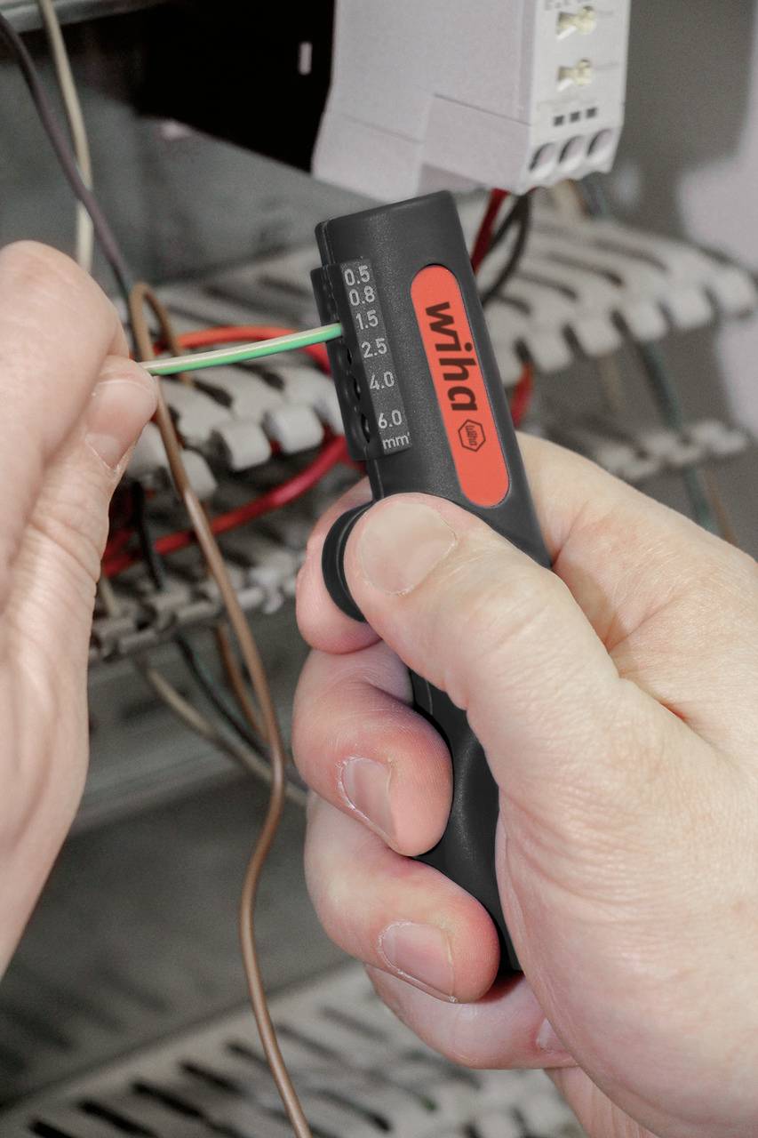 Ein Mensch verwendet ein Kabelschneider-Werkzeug, um ein Kabel in einem Schaltschrank zu isolieren.