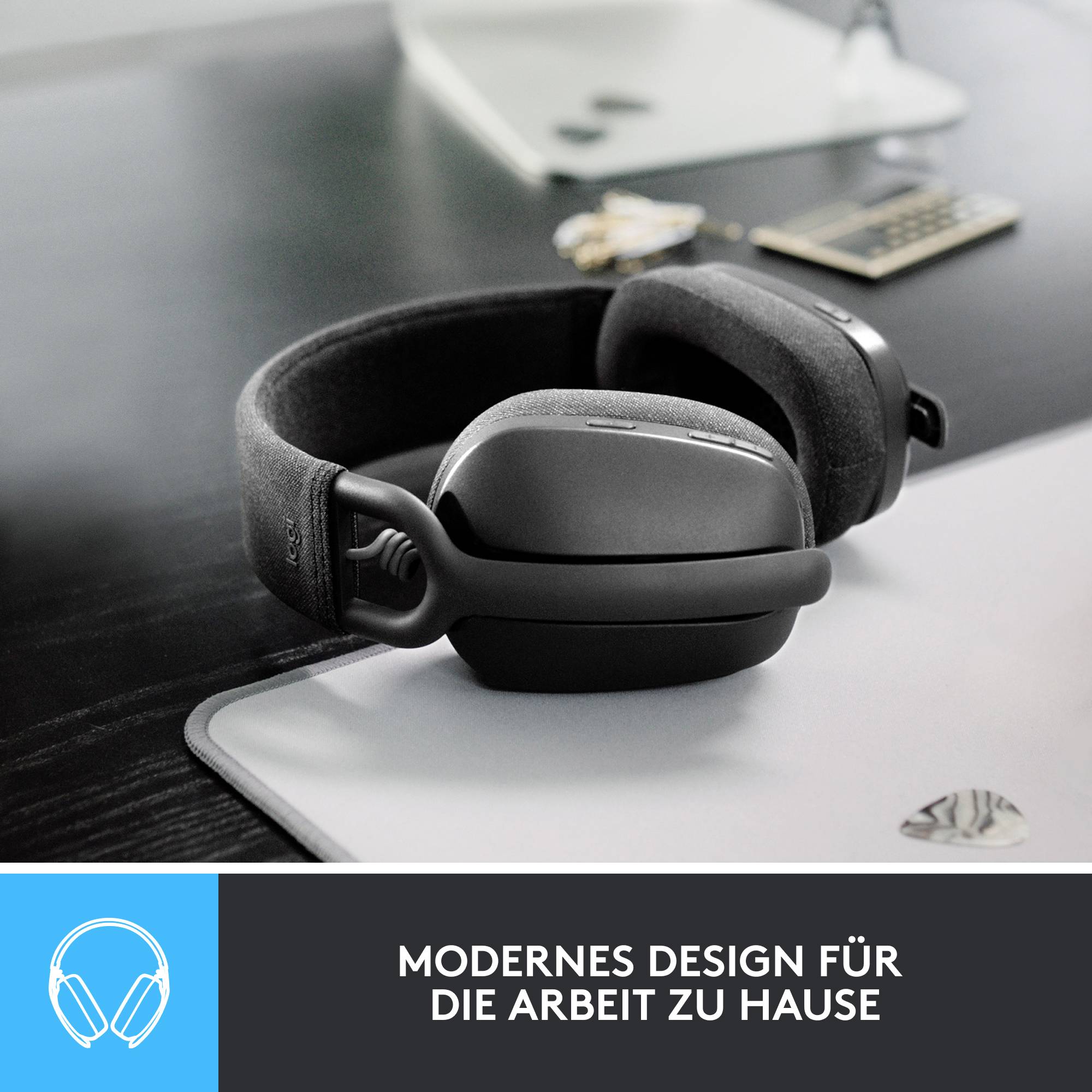 Ein schwarzer Kopfhörer liegt auf einem Schreibtisch. Im Hintergrund sind ein Computer und eine Tastatur zu sehen. Text: 'Modernes Design für die Arbeit zu Hause'.