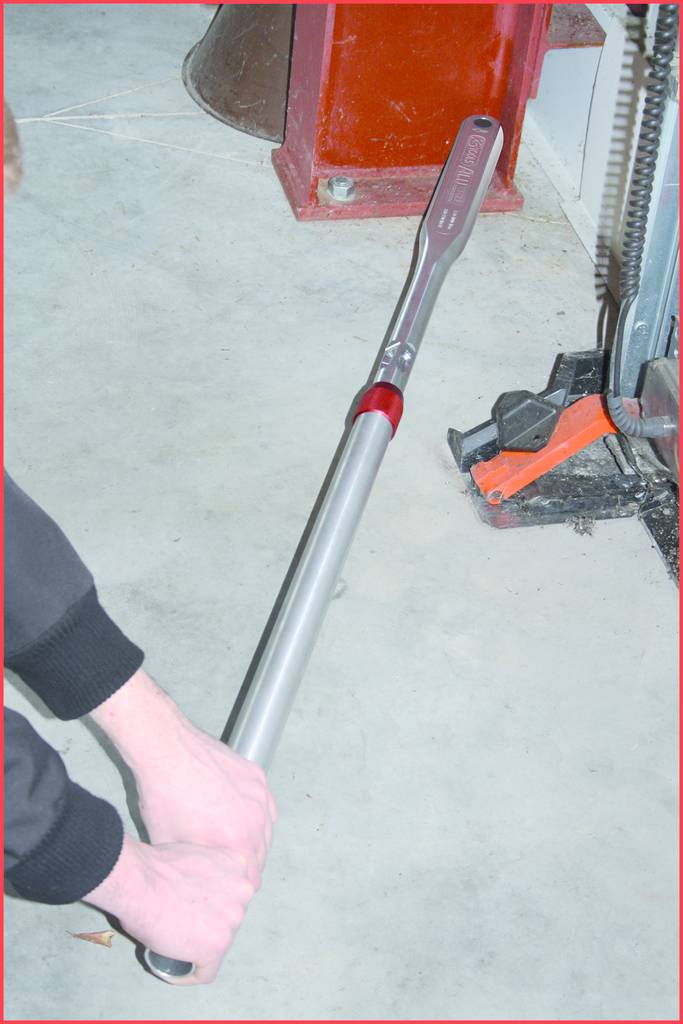 Eine Person hält einen langen, metallischen Drehmomentschlüssel in der Hand und zieht eine Schraube an einer Maschine fest.