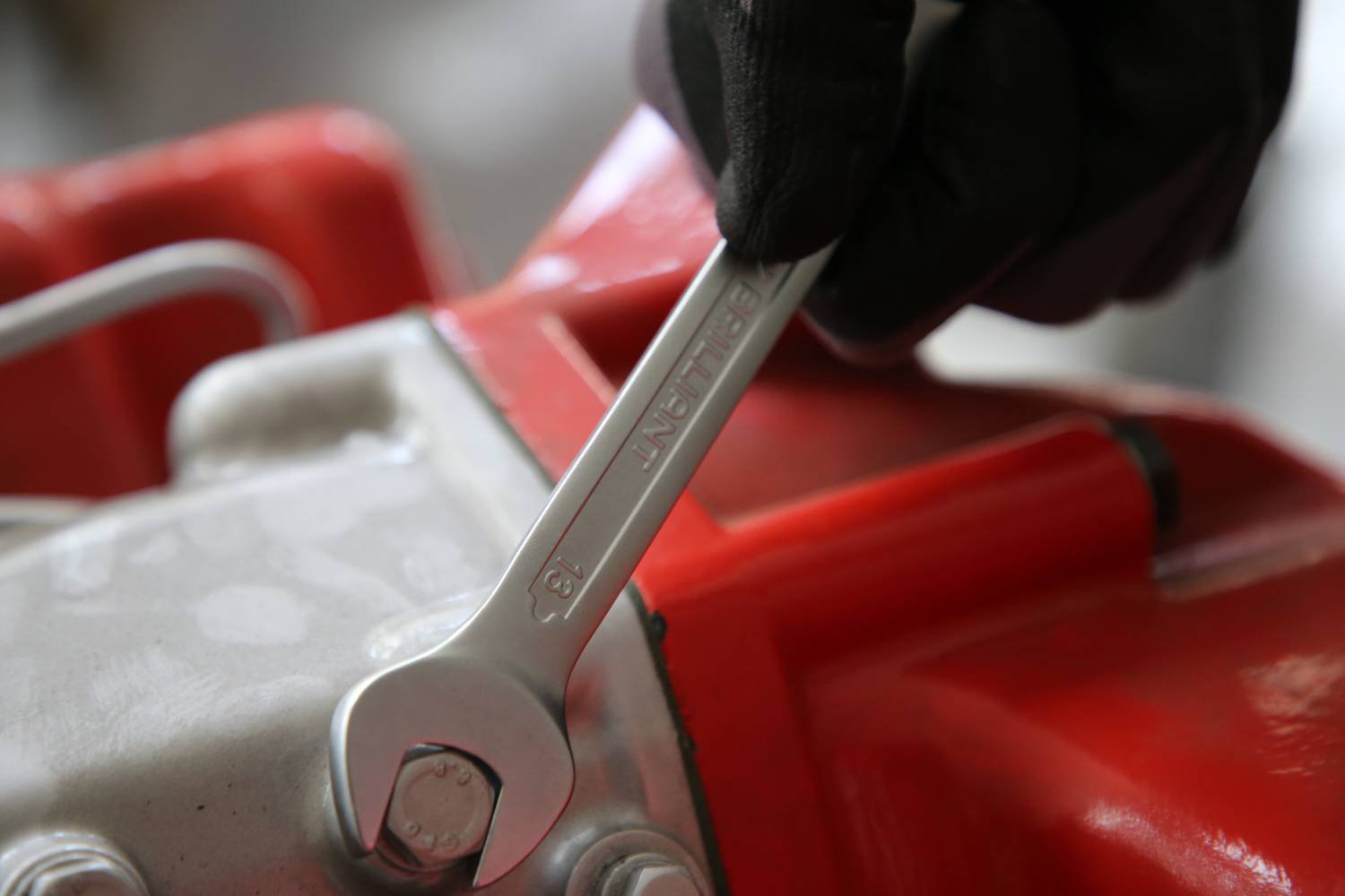 Eine Person zieht mit einem Schraubenschlüssel eine Schraube an einem roten mechanischen Gerät fest.
