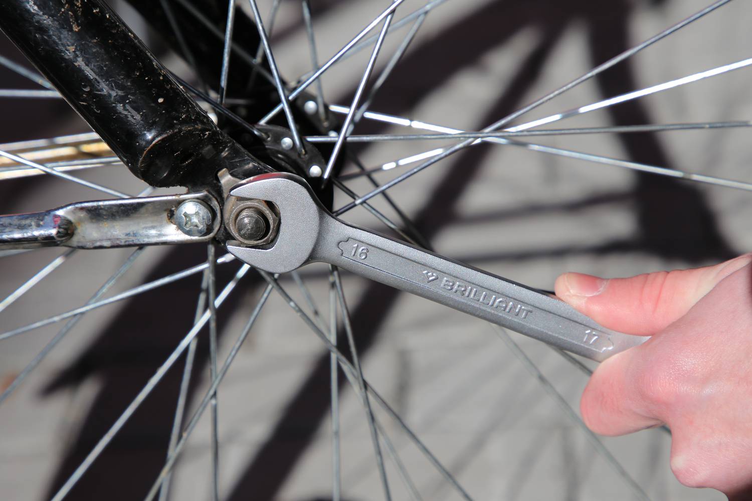 Eine Hand hält einen Schraubenschlüssel und zieht die Mutter einer Fahrradachse an. Die Speichen des Rads sind im Hintergrund sichtbar.