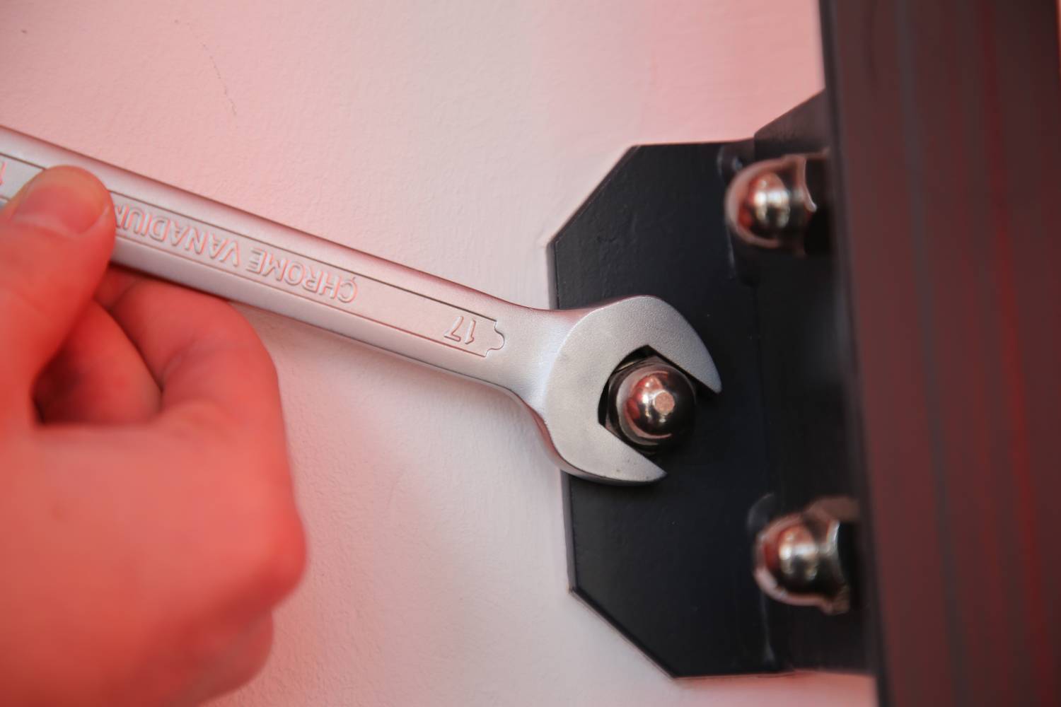 Eine Hand zieht mit einem Schraubenschlüssel eine Mutter an einer schwarzen Metallhalterung fest.