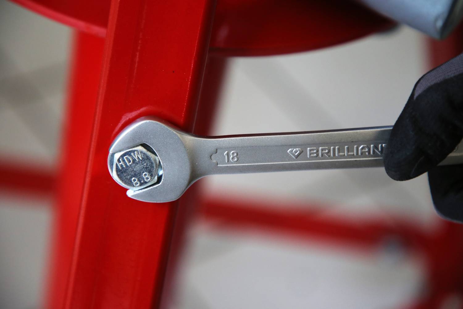 Ein Schraubenschlüssel der Größe 18 wird von einer behandschuhten Hand gehalten, neben einem roten Metallrohr platziert.