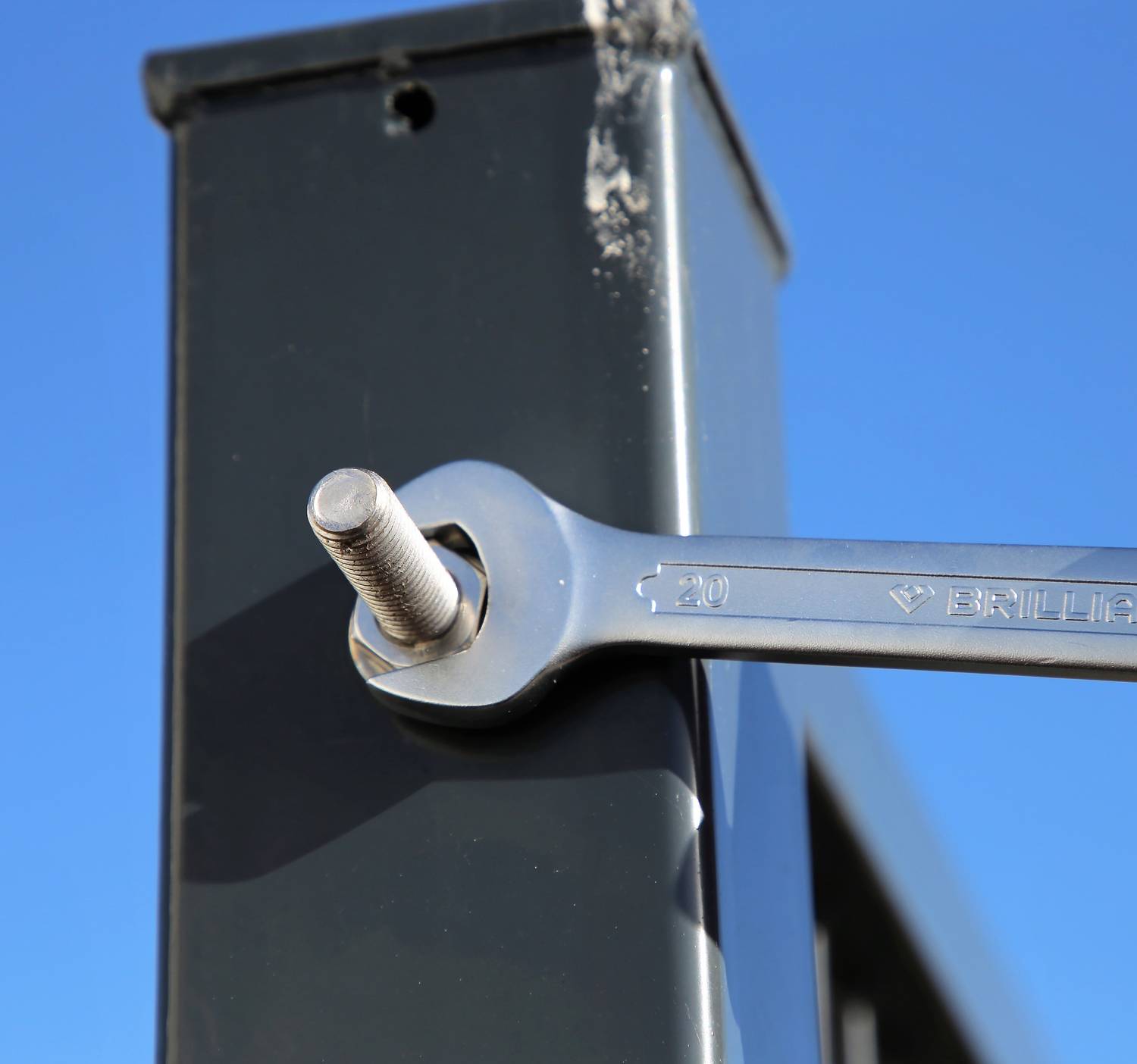 Ein Schraubenschlüssel zieht eine Schraube an einem Metallrahmen fest. Der Himmel ist blau im Hintergrund, keine weiteren Details sichtbar.