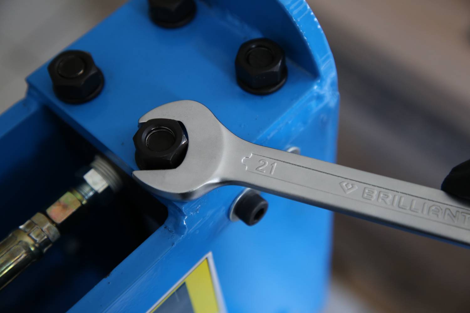 Ein Schraubenschlüssel zieht eine Mutter an einer blauen Metallmaschine an. Der Schraubenschlüssel hat die Aufschrift '21 Brilliant'.