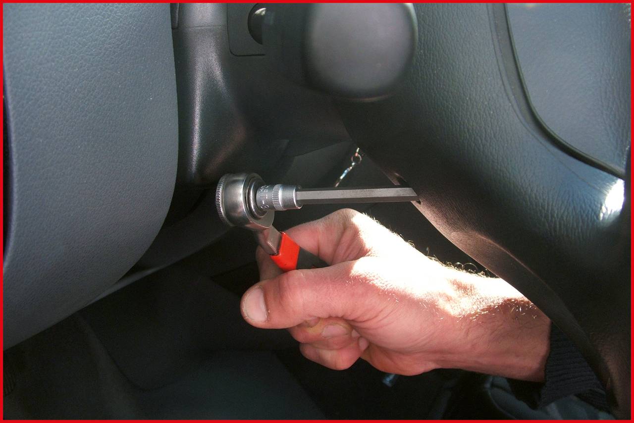 Eine Hand hält ein Werkzeug, das in das Zündschloss eines Autos eingeführt ist, als würde es manipuliert. Innenansicht eines Fahrzeugs.