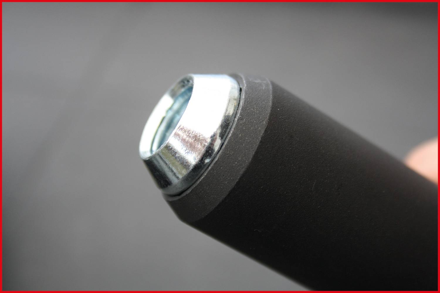 Nahaufnahme eines runden, schwarzen Metallrohrs mit silberner Kappe an einem Ende. Fokus auf das Kappen-Detail, unscharfer Hintergrund.