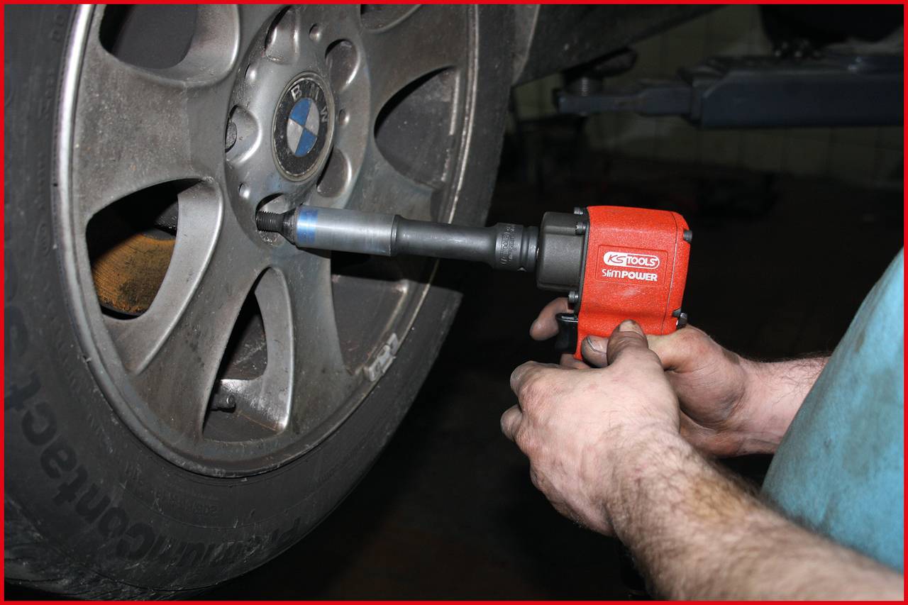 Eine Person wechselt mit einem Schlagschrauber einen Autoreifen in einer Werkstatt. Der Reifen gehört zu einem Fahrzeug mit Aluminiumfelgen.