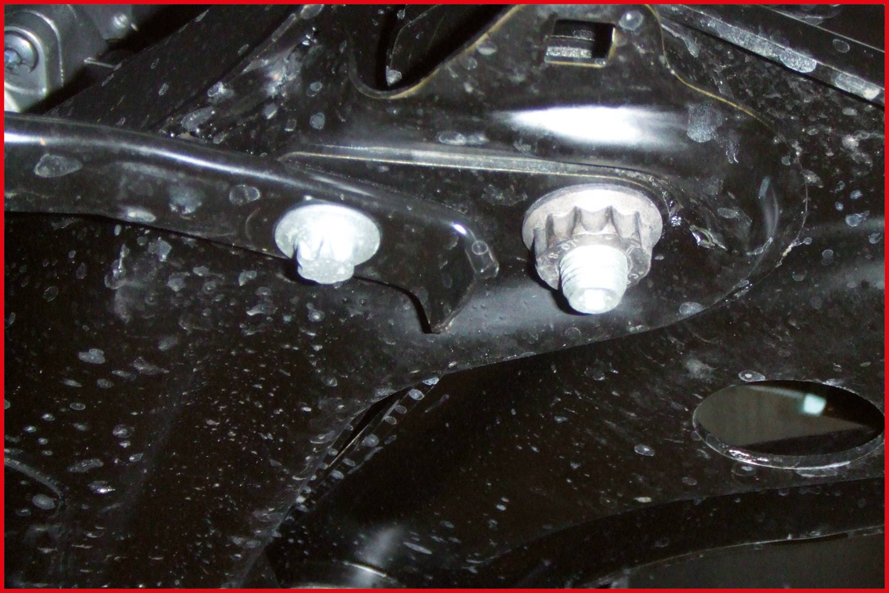 Eine Nahaufnahme eines schwarzen Metallteils mit Schrauben und einer gebogenen Halterung. Die Oberfläche ist mit Wasserflecken bedeckt.