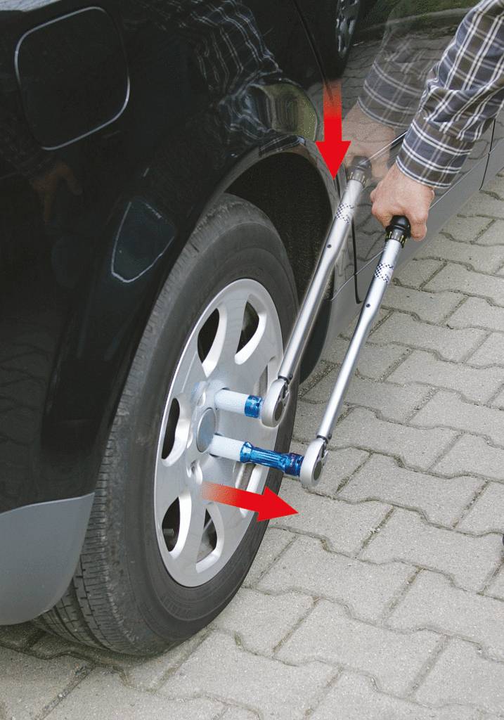 Mann zieht Radmuttern eines Autos mit zwei Kreuzschlüsseln an.