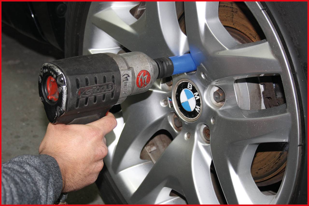 Eine Hand setzt einen Schlagschrauber an eine Autoreifenmutter an einem BMW-Auto an, um die Radschrauben zu lösen oder festzuziehen.