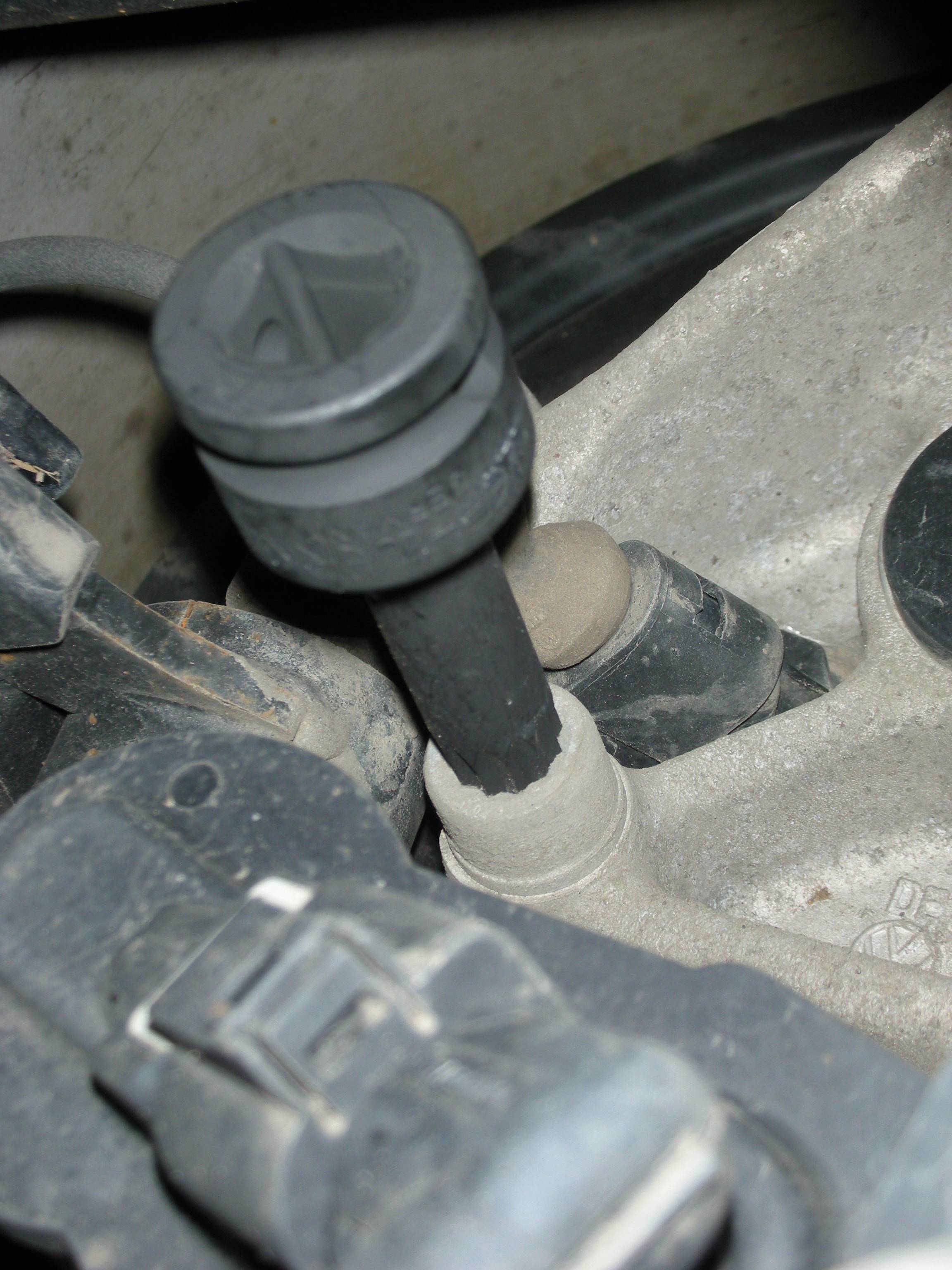Nahaufnahme eines schwarzen Autoteils mit einem Hebel auf einer Metalloberfläche, möglicherweise Teil eines Getriebes oder einer Motorverbindung.