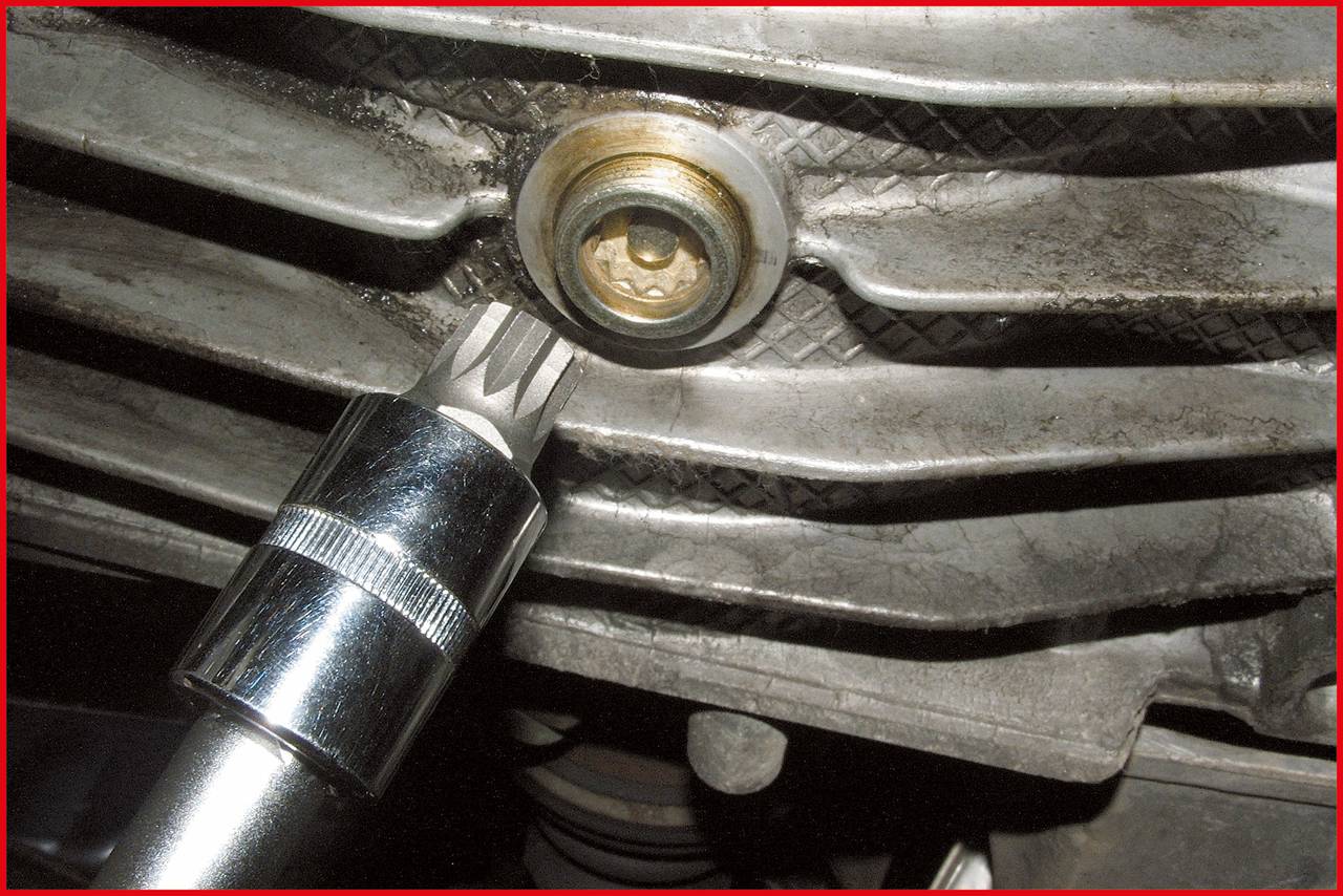 Ein Werkzeug wird verwendet, um eine Schraube an einem metallischen Bauteil zu lösen. Die Oberfläche ist verschmutzt und abgenutzt.