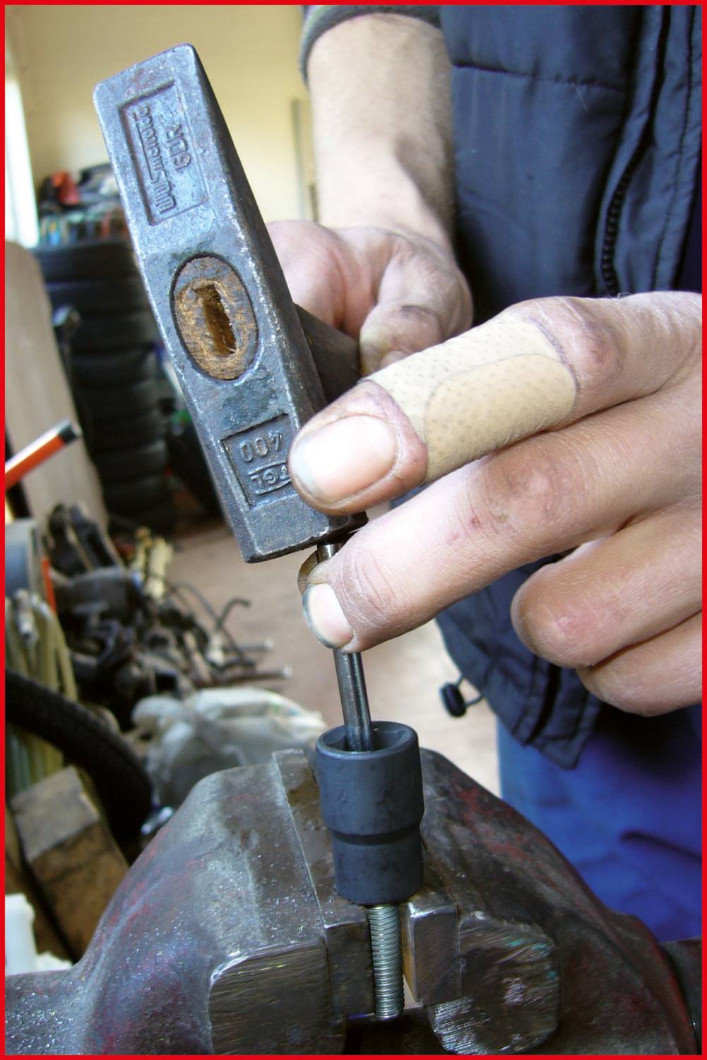 Eine Hand hält einen Metallstempel, während ein Daumen mit Pflaster einen Schraubstock für die Bearbeitung von Metall oder Holz fixiert.