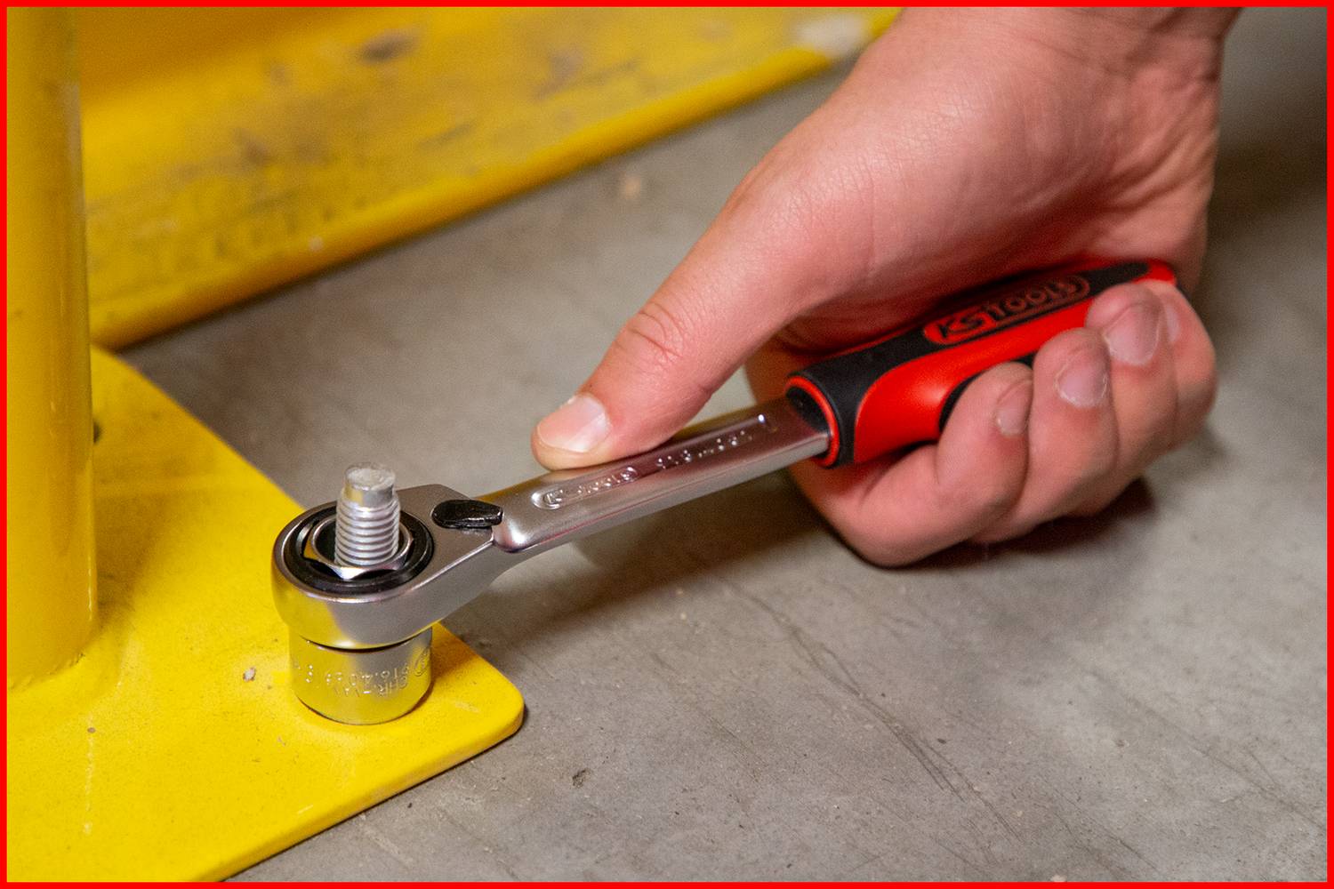 Eine Hand benutzt einen Steckschlüssel, um eine Schraube an einer gelben Metallstruktur festzuziehen.