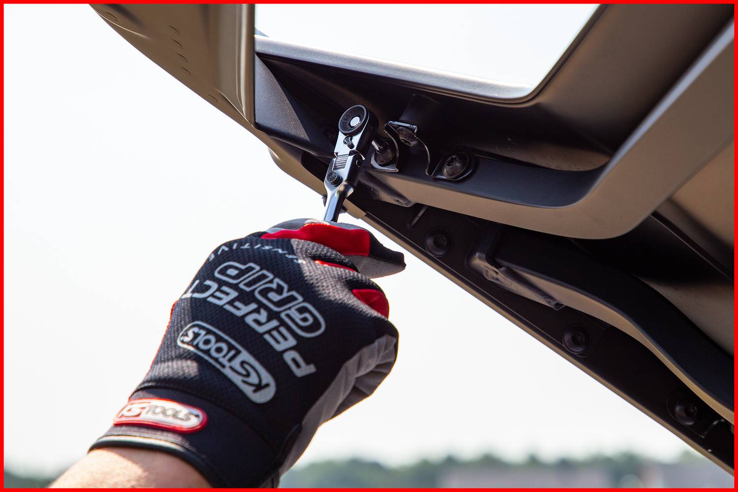 Hand in Arbeitshandschuh montiert Autoteil mit Ratsche, Sonnenlicht im Hintergrund.