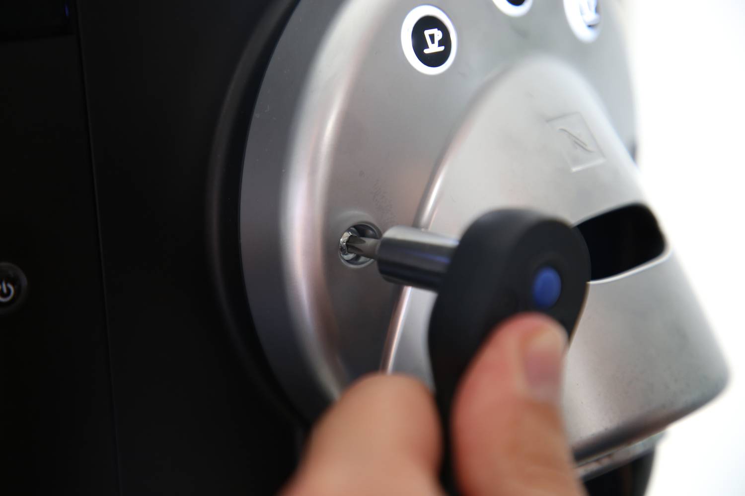 Eine Hand steckt einen Schlüssel in ein Schloss auf einer Kaffeemaschine. Die Maschine hat Tasten mit Kaffeetassen-Symbolen.