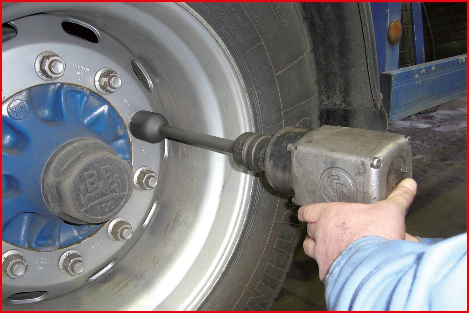 Ein Mechaniker zieht mit einem Schlagschrauber die Schrauben eines Lastwagenrads an. Der Reifen und das Werkzeug sind im Fokus.