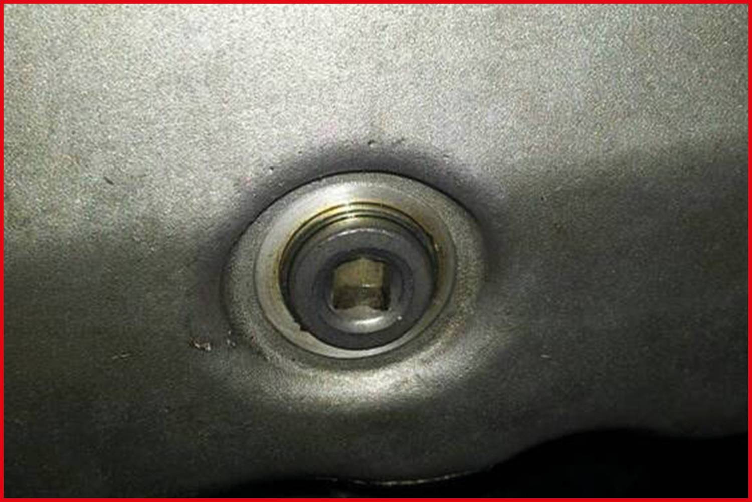 Nahaufnahme eines Metallstopfens in einer Maschine oder einem Gerät, zeigt eine sechseckige Öffnung zur Wartung oder Reparatur.