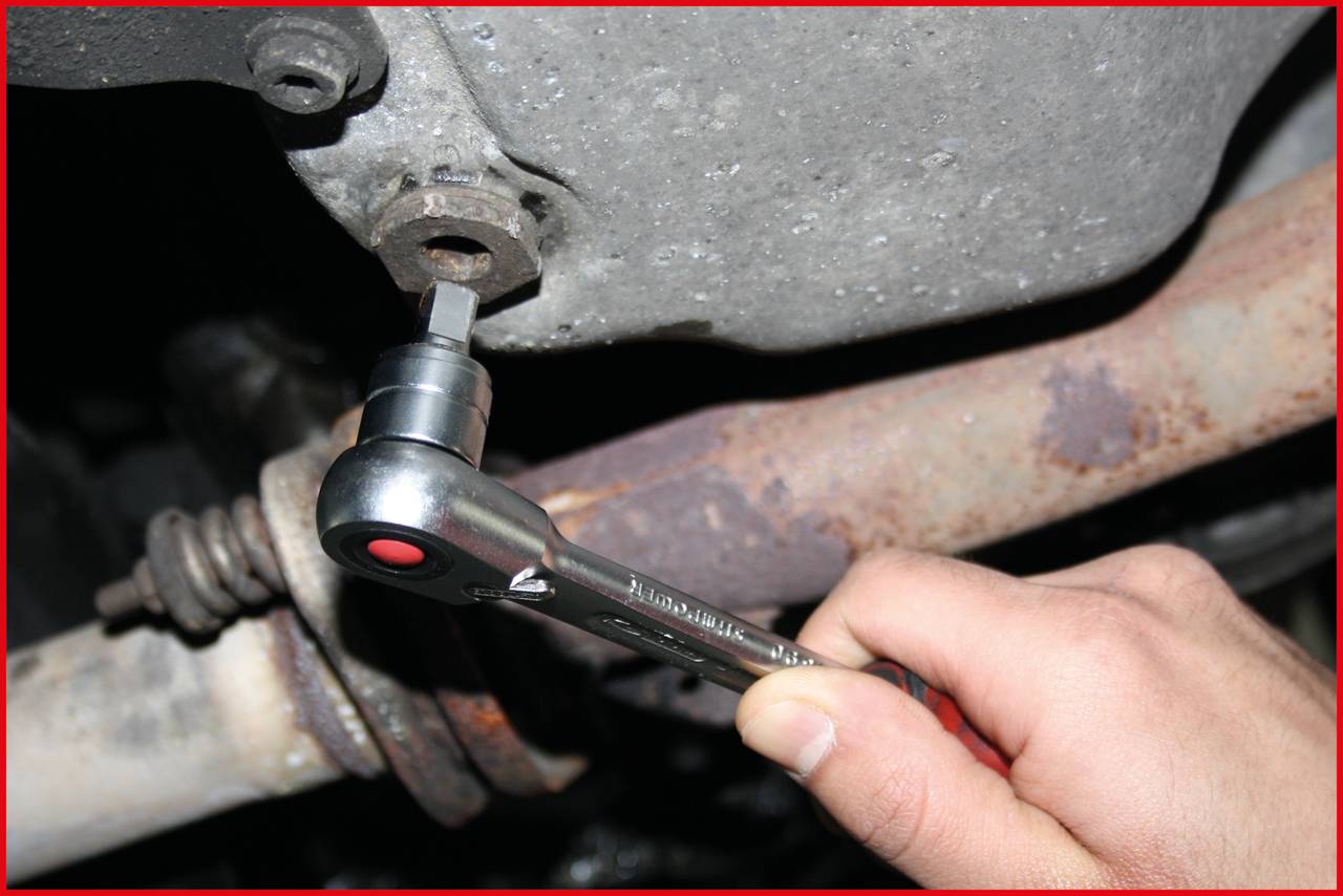 Eine Hand mit Ratsche zieht eine Schraube an einem Auto fest.