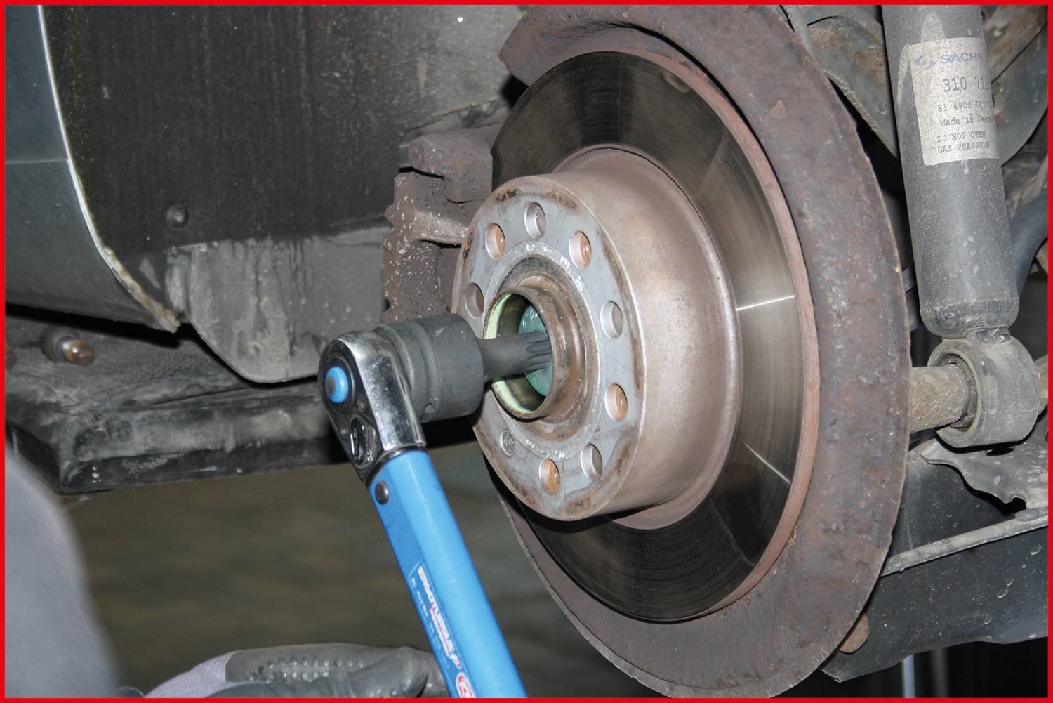 Ein Mechaniker zieht mit einem Drehmomentschlüssel eine Schraube an einer Bremsscheibe am Auto an.
