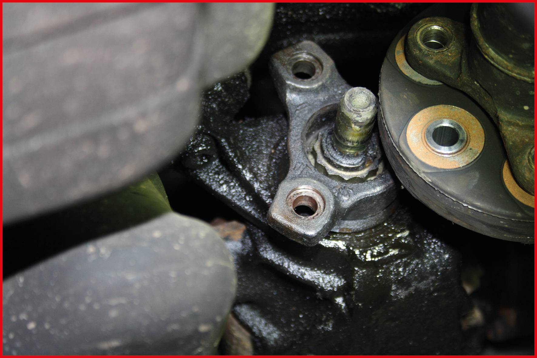 Ein Nahaufnahme einer Autokomponente, vermutlich Teil der Aufhängung oder Lenkung, zeigt Bolzen und Metallteile mit sichtbarem Verschleiß.