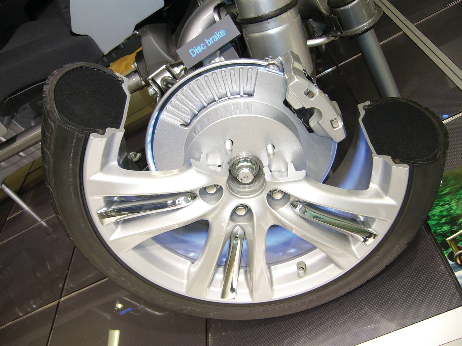 Teil eines Fahrzeugreifens mit sichtbarer Bremsscheibe und Bremssattel. Das Rad ist teilweise durchschnitten, um die Mechanik zu zeigen.