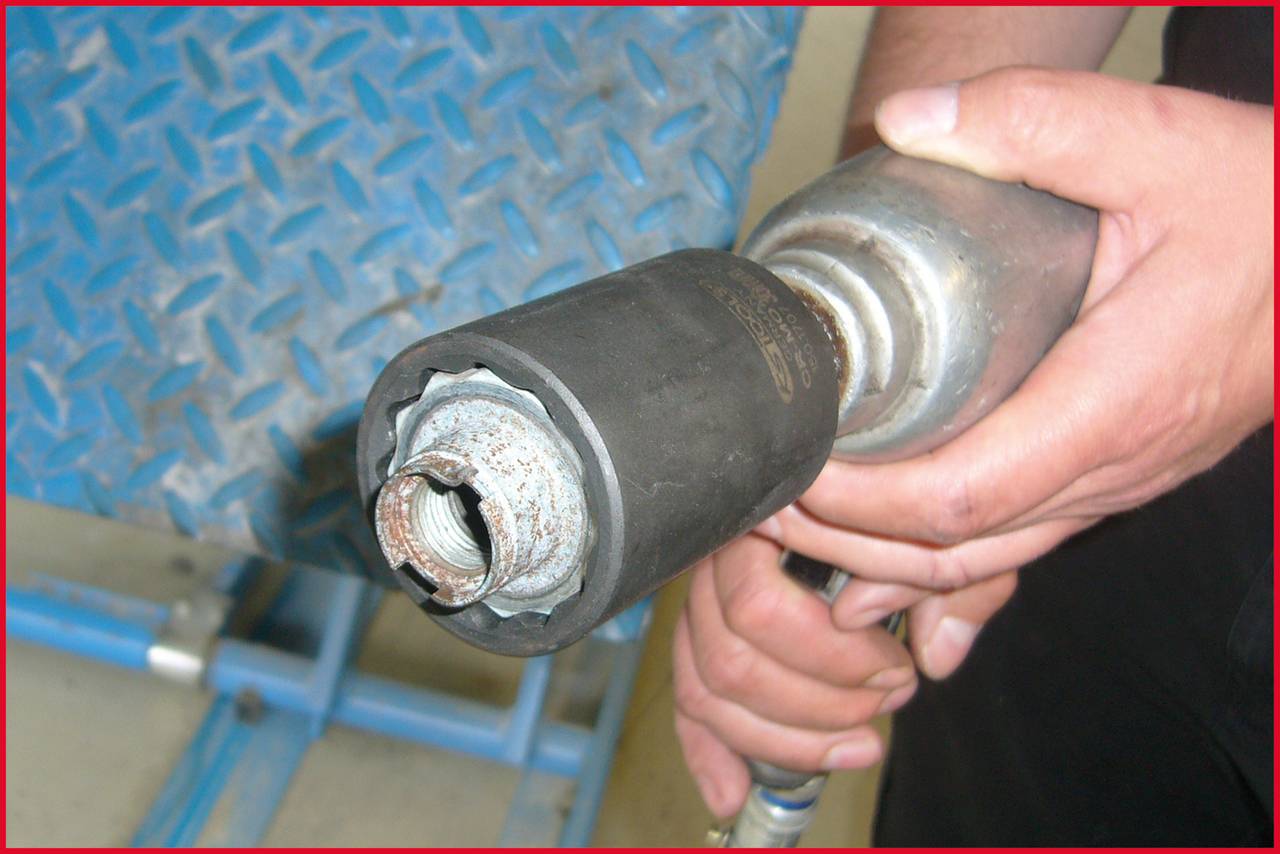 Eine Person hält eine Metallvorrichtung mit einer rostigen Mutter an der Spitze, bereit zur Verwendung auf einer blauen Metalloberfläche.