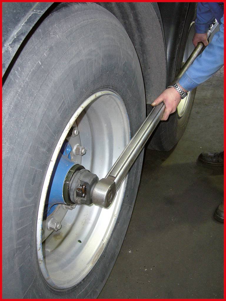 Eine Person zieht mit einem großen Drehmomentschlüssel die Radmuttern eines Lkw-Reifens an.