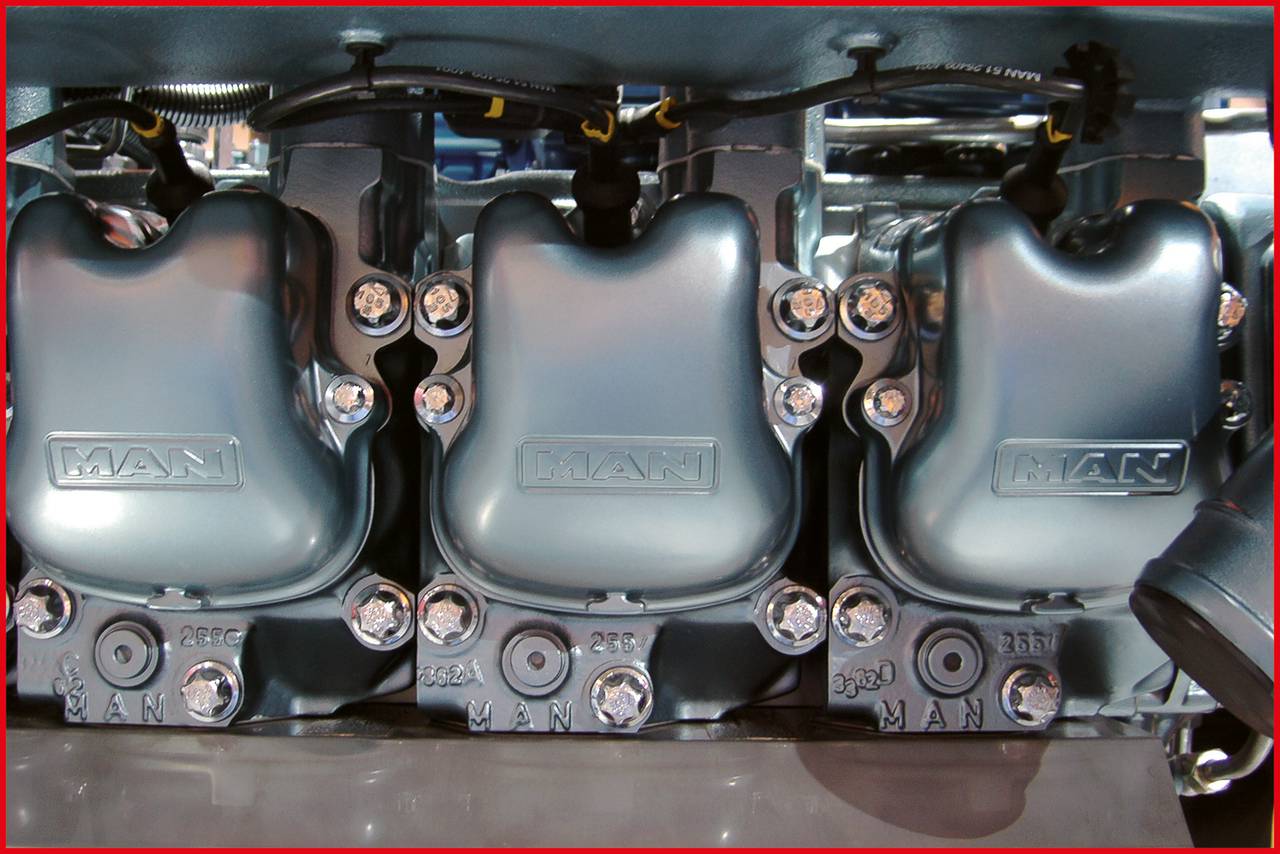 Nahaufnahme eines industriellen Maschinenmotors mit drei metallischen Gehäusen, darauf graviert 'MAN'. Mechanische Details sind sichtbar.