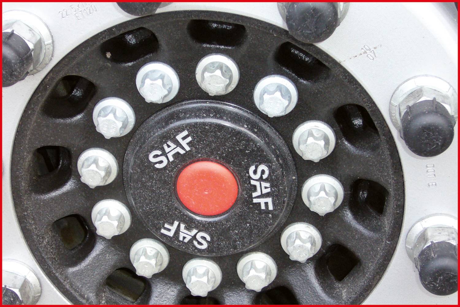 Nahaufnahme eines schwarzen Reifenrads mit silbernen Muttern und einem roten Mittelknopf, auf dem 'SAF' steht.