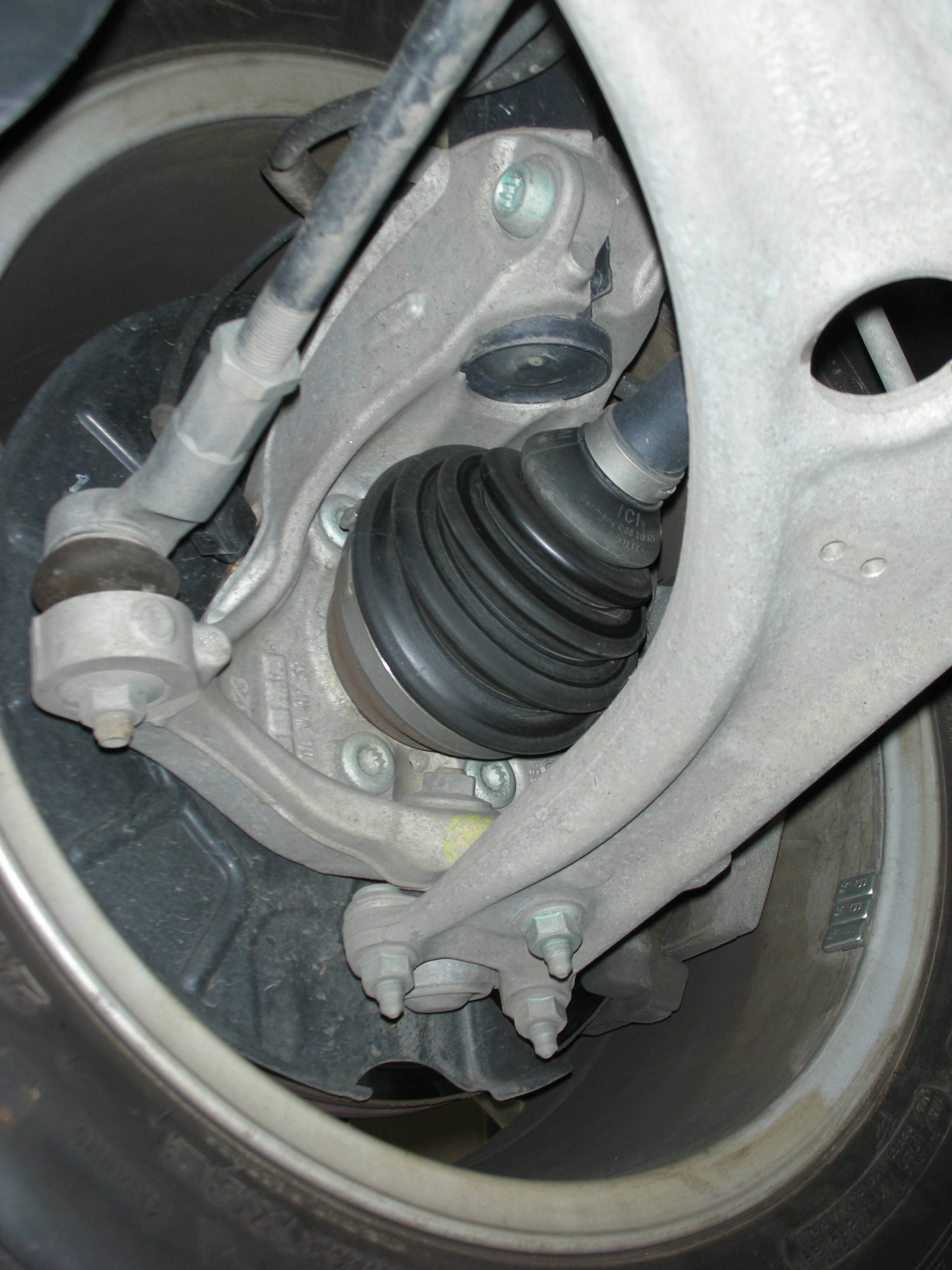 Nahaufnahme einer Autoaufhängung mit Achsmanschette und Verschraubungen. Sicht auf das Radlager und die Aufhängungsmechanik.