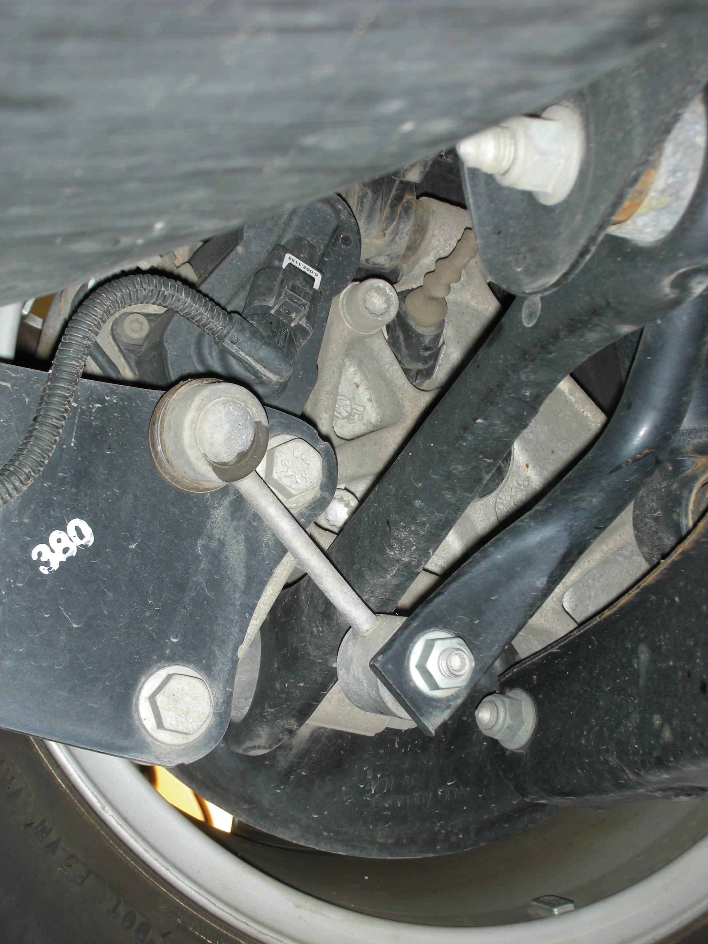 Untersicht einer Fahrzeugaufhängung mit Dämpfer, Feder und Querlenker. Zentrales Metallteil mit Schraube befestigt.