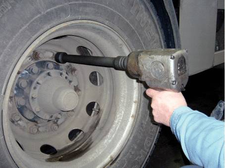 Eine Person zieht mit einem Schlagschrauber die Radmuttern eines LKW-Reifens fest.