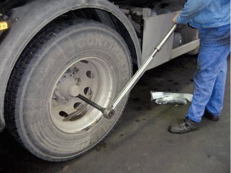 Eine Person benutzt einen langen Hebel, um die Radmuttern eines großen LKW-Reifens zu lösen. Der Reifen ist stark verschmutzt.