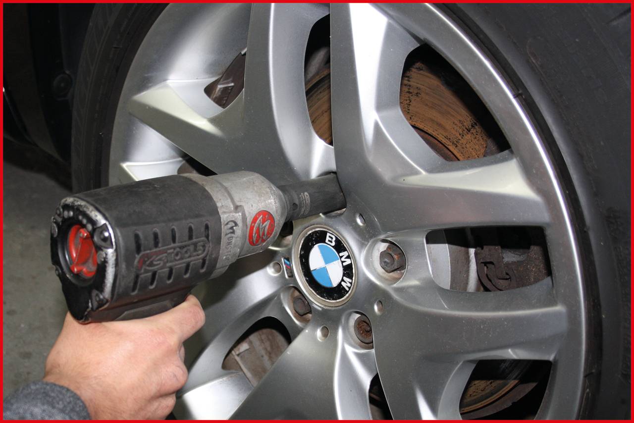 Eine Hand verwendet einen elektrischen Schlagschrauber, um eine Schraube an einem Autoreifen mit BMW-Logo zu befestigen.