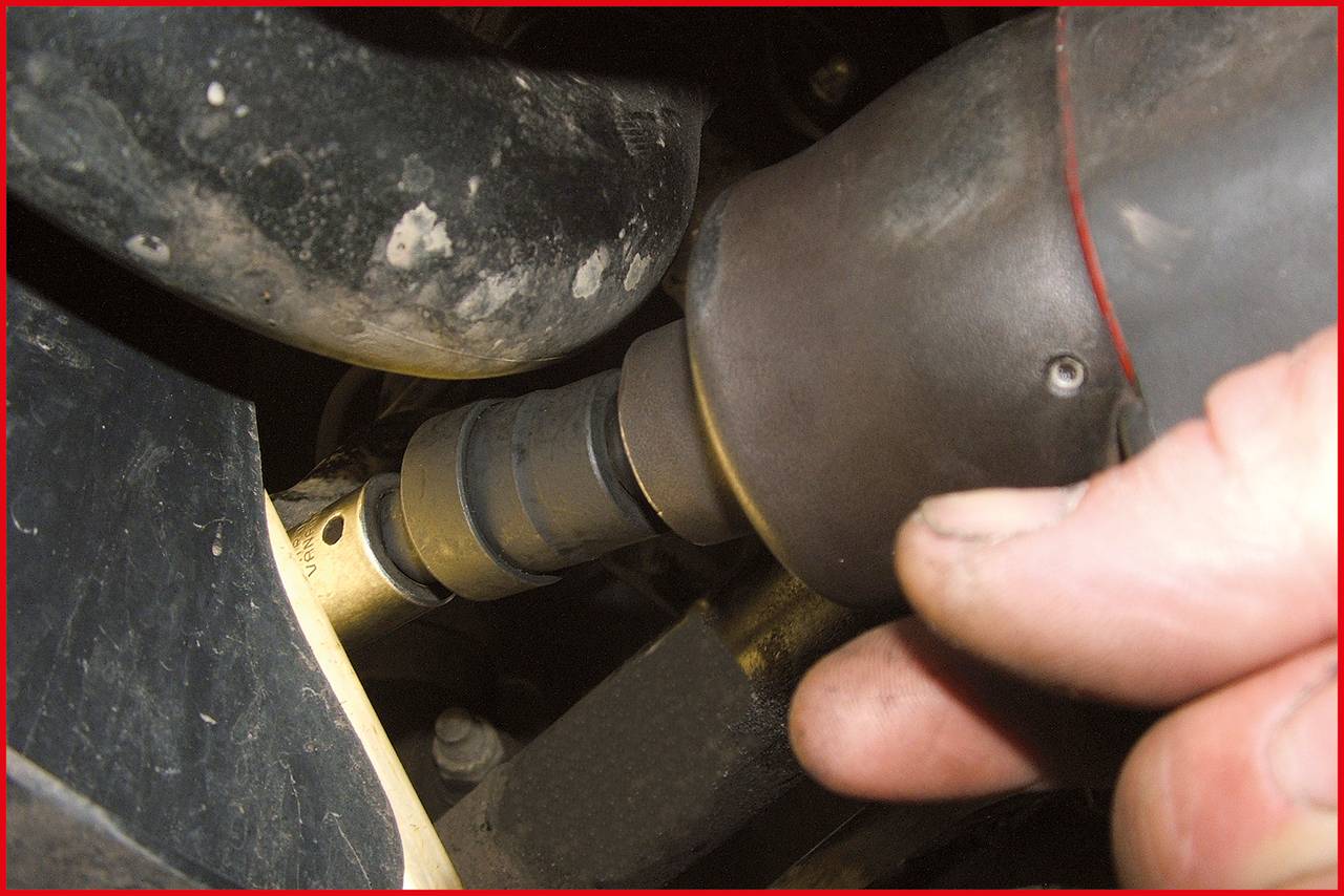 Nahaufnahme einer Hand, die ein elektrisches Werkzeug benutzt, um eine Schraube an einem Metallteil zu befestigen. Umgebung zeigt Fahrzeugteile.