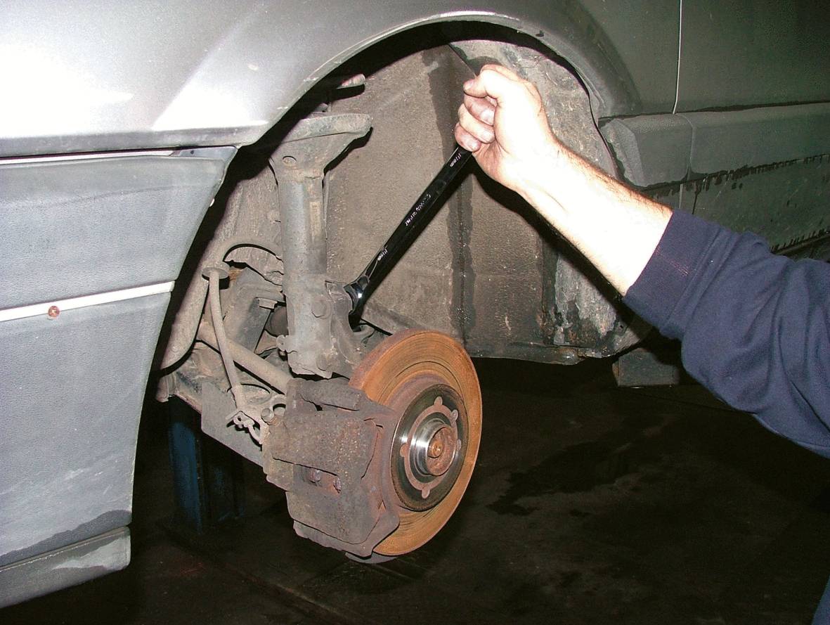 Eine Person repariert ein Auto-Radbremsensystem mit einem Schraubenschlüssel in einer Werkstatt.