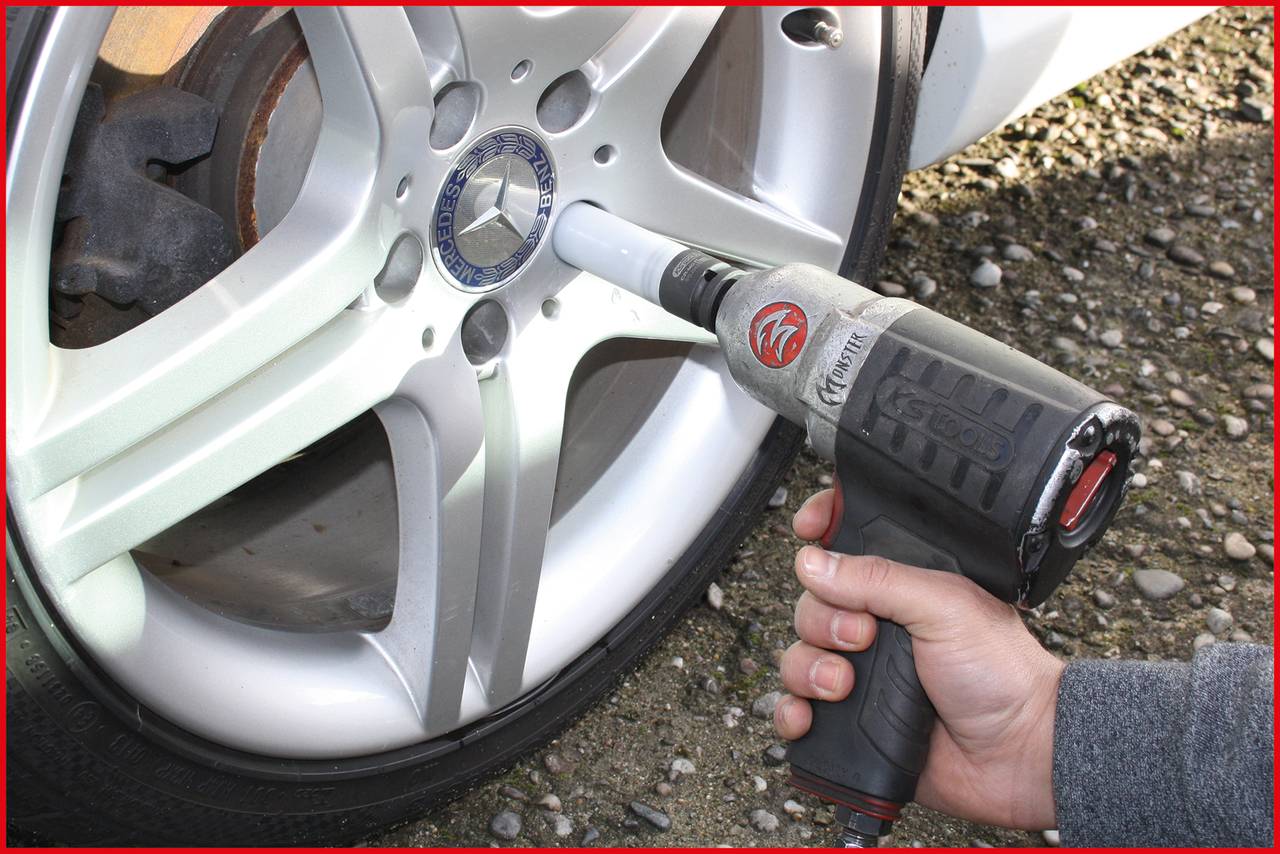 Eine Hand benutzt einen Schlagschrauber, um die Radschrauben eines Autoreifens mit silberner Felge festzuziehen.